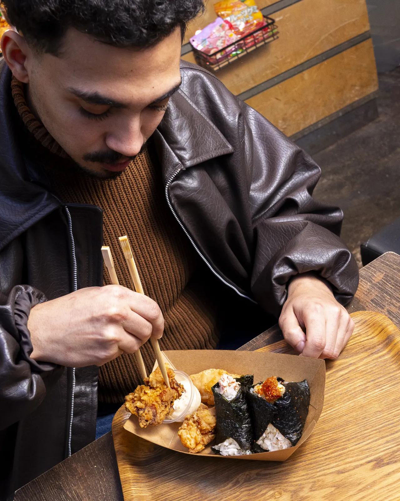Vue de dessus : un client attrape un onigiri dans sa barquette garnie de karaage, baguettes à la main