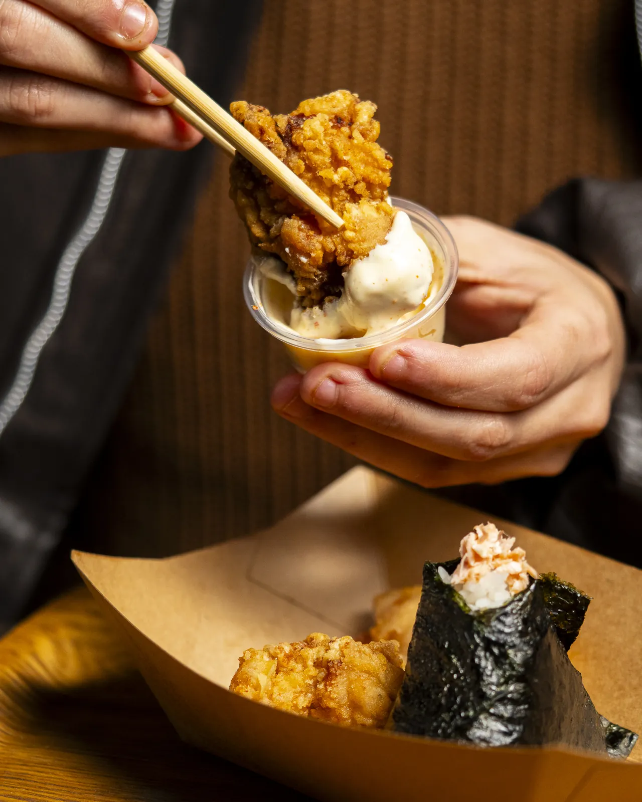 Gros plan sur un karaage trempé dans la sauce et un onigiri au saumon dans sa barquette kraft