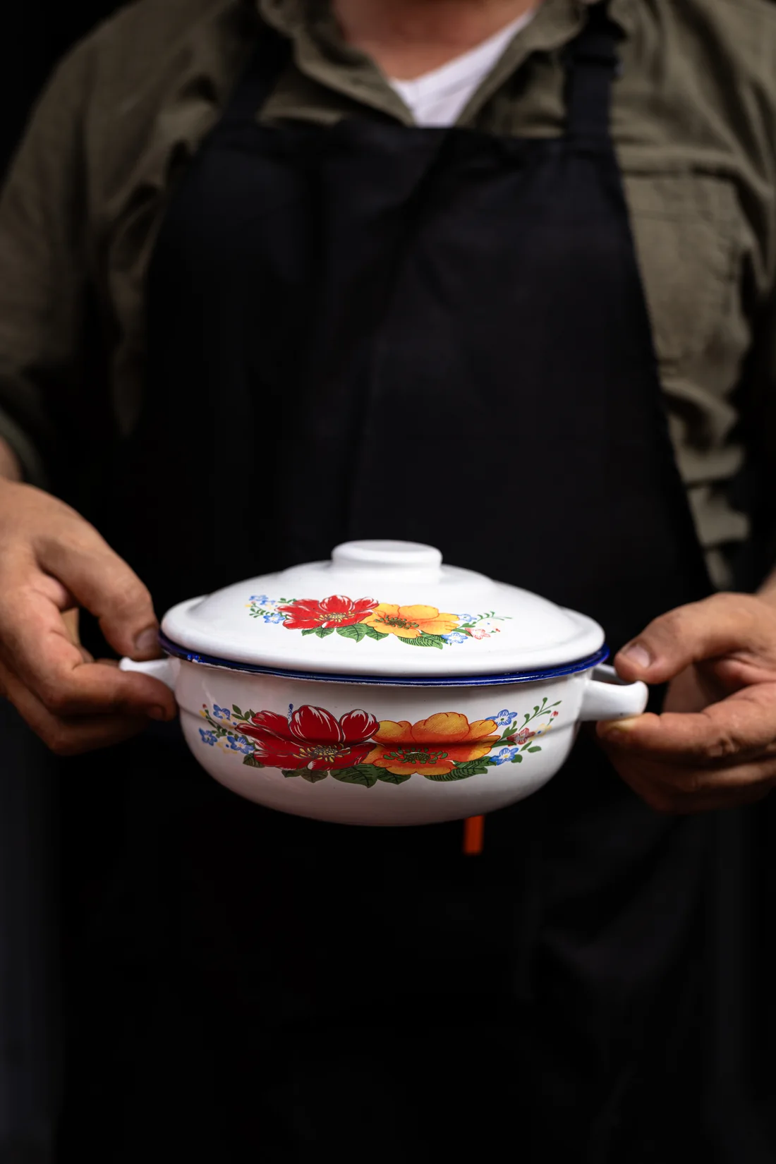 Un cuisinier des Petites Cocottes présente à deux mains une cocotte émaillée de nouilles